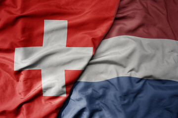 big waving national colorful flag of switzerland and national flag of netherlands .