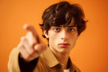 Fototapeta premium Close-up portrait photography of a tender boy in his 20s pointing empty space against a beige background. With generative AI technology
