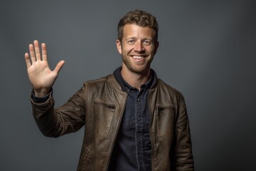 Lifestyle portrait photography of a grinning boy in his 30s making a no or stop gesture with the extended palm against a cool gray background. With generative AI technology