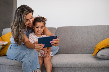 mother and little daughter at home looking at a digital tablet - video call, social media -