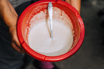 A woman, a cook, holds in her hands a red plastic bowl with batter, dough for baking. Food photography, top view, concept.