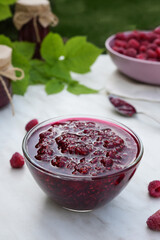 Fresh raspberries and jam with blurred green background. Concept of cooking raspberry jam on white marble table. Banner, menu, recipe. Side view. Selective focus.