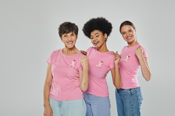 breast cancer awareness, joyful multicultural women smiling on grey backdrop, different generations