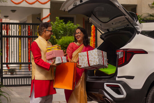 Senior couple unloading Diwali gifts from car trunk after shopping