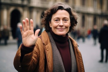 Close-up portrait photography of a jovial mature woman waving hello or goodbye dressed in a classic turtleneck at the uffizi gallery in florence italy. With generative AI technology