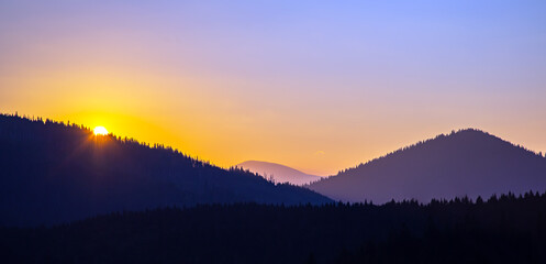 Colorful clouds in the sky at sunset against the backdrop of a mountainous forest area.