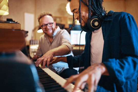 Smiling musician playing keyboards with his producer in a studio