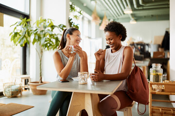 Two diverse friends in sportswear laughing over coffee after a workout