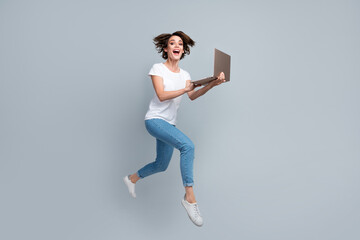 Full length photo of cute woman wear stylish t-shirt denim pants hold laptop hurry run in empty space isolated on gray color background