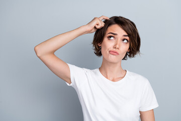 Photo of doubtful unsure lady wear white t-shirt finger head looking empty space isolated grey...