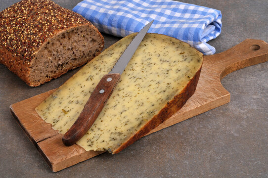 Morceau de tomme &agrave; l'ail des ours avec un couteau sur une planche &agrave; d&eacute;couper en bois et un pain aux graines