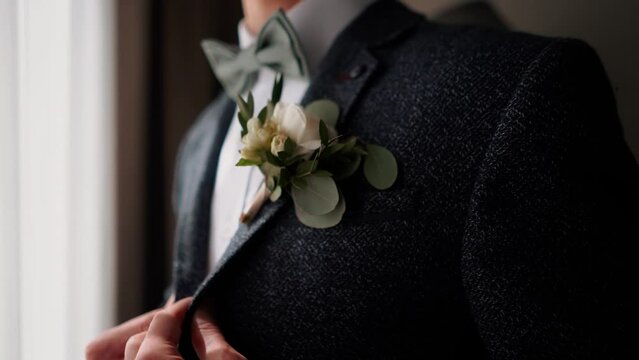 Solid handsome man groom in a business suit jacket straightens his tie in the morning before his wedding