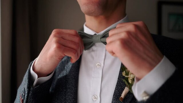 Solid handsome man groom in a business suit jacket straightens his tie in the morning before his wedding