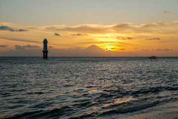 Fototapeta premium sunset view on senggigi lombok beach with the silhouette of mount agung bali, sunset over the sea, sunset at the beach, sunset and mountain, lighthouse at sea