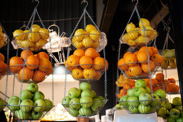 Various type of fresh fruits hang on steel basket in frui juice stall. Apple, Orange and Lemon on steel basket