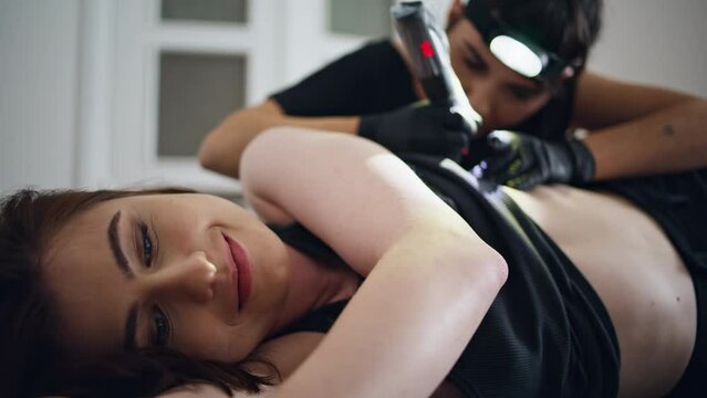 Happy woman getting tattoo home salon close up. Smiling client girl laying couch