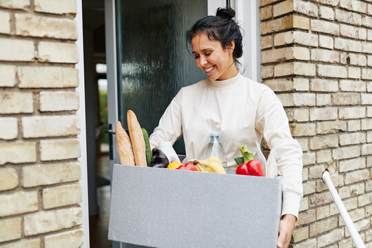 Smiling woman carrying groceries into her home