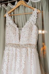 Close-up of a handmade wedding dress on a wooden hanger with embroidered flowers. Near the dress with open shoulders without sleeves