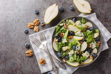 Blueberries, pear, leafy greens salad with walnuts and blue cheese close-up in a plate on the table. horizontal top view from above