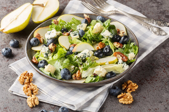 Gourmet salad with sweet pears, blueberries, blue cheese, lettuce and walnuts close-up in a plate on the table. Horizontal
