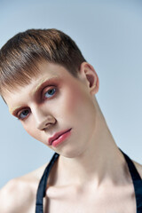 portrait, androgynous person with makeup looking at camera on grey, beauty and visage, queer