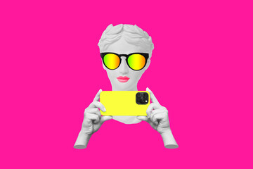 Antique statue's head in sunglasses holding yellow mobile phone with photo camera in hands taking...