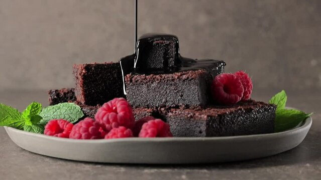 Pouring melted black chocolate on brownie cake. Chocolate cake and fresh raspberries on a rustic plate.