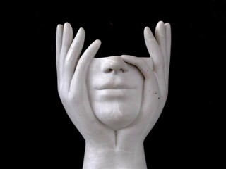 White plaster sculpture with face covered by hands on black background – concept of silence and...