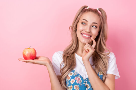 Photo of cute positive minded person finger touch lips hand hold apple look empty space isolated on pink color background