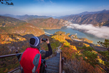 Fototapeta na wymiar tourist with backpack admiring landscape in Autumn In the morning, a sea of ​​mist flows through the river in the valley In the autumn at Jebibong of Waraksan Mountain National Park, South Korea.