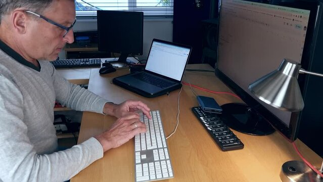 A man working from his home office on a laptop and external monitor