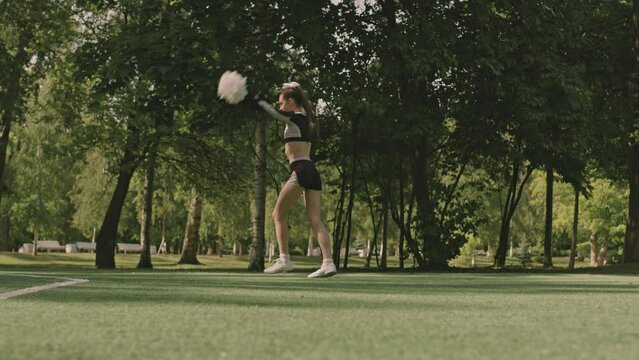 Wide shot of young cheer girl with pompoms performing front handspring on soccer field outdoors