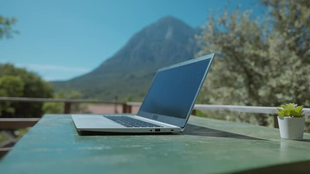 remote freelancer workplace with laptop on table outdoors on wooden terrace in nature. campsite and bungalow with terrace in amazing place with view on mount, hills and green woods at sunny day.