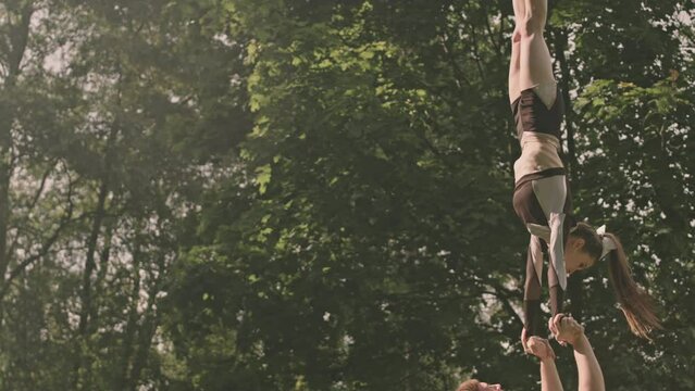 Tilt up shot of base athlete holding flyer girl above his head while she performing split handstand on outdoor soccer field