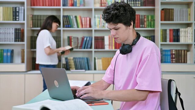 Young male student sitting with laptop with books in college library