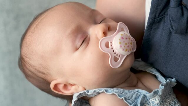 Caucasian one month baby girl with a pacifier sleeping in her mother arms.