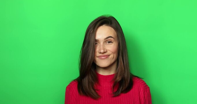 Playful female demonstrate gesture quite showing forefinger on green studio background. Smiling woman having secrecy saying hush or shh with finger on lips. Concept of gossip, secret.