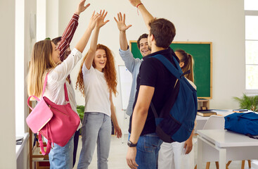 Team of happy students high five each other. Group of cheerful young people standing in the school classroom and giving each other a high five. Teamwork, fun, education concept