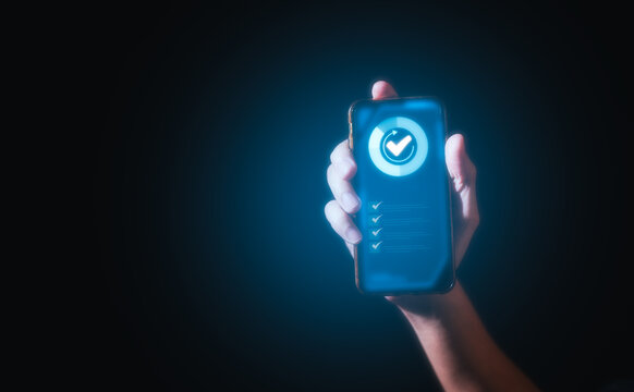 businessman Hand holding a smartphone with a green checkmark icon on the screen to show a validated, confirmed, completed or approved status