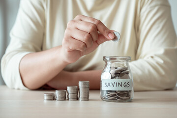 Woman placing coin into a jar of saving money to achieve financial goals through patience and effort