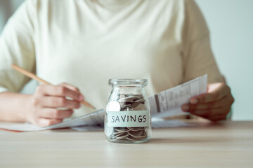 A woman's hands placing coins into a glass jar, the act of saving money to pay bills.