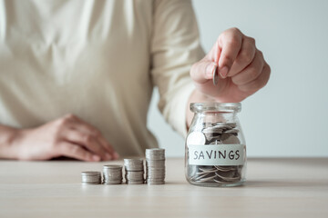 Woman placing coin into a jar of saving money to achieve financial goals through patience and effort