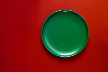 Green plate on a red background. Minimalistic concept of the winter holidays - Christmas and New Year. Top view. Space for text