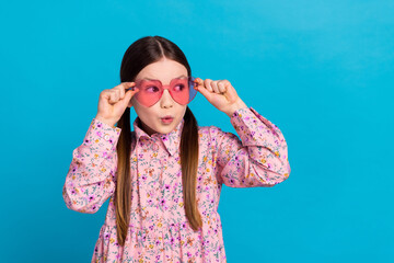 Photo portrait of pretty schoolkid touch pink heart sunglass dressed stylish pink flower print outfit isolated on blue color background