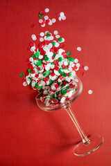 Confetti in a champagne glass on a red background. The concept of the winter holidays - Christmas and New Year. Top view. Space for text