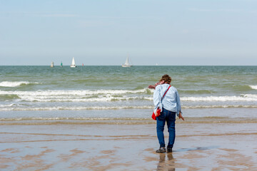 Femme de dos marchant sur une plage de la mer du Nord et voiliers dans le lointain