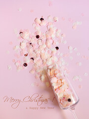 Confetti in a champagne glass on a pink background with text - Merry Christmas and Happy New Year. The concept of the winter holidays - Christmas and New Year. Top view
