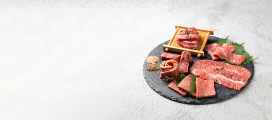Top view Variety Fresh raw beef steaks on natural black stone plate for grilling. hot pepper and herbs. Japanese food isolated on gray stone banner background