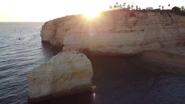 Descending Aerial View of Ocean and Rocky Beach Shore Line with Sun Leaks. Sun beaming through till the camera focuses with a boat moving towards the camera.