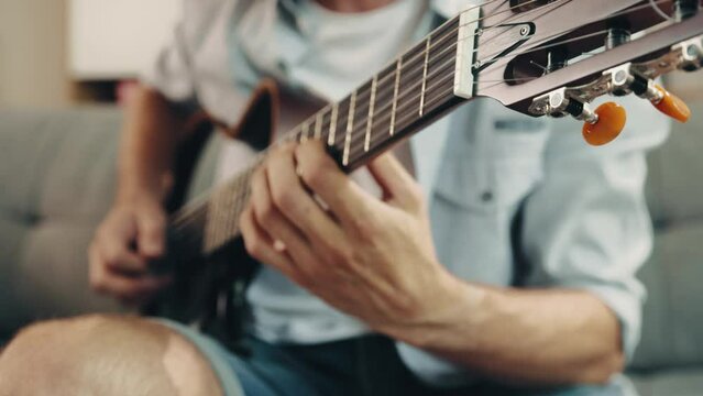 Close-up of male hands playing electric guitar. Man in casual clothes sitting on sofa and learning new songs melodies. Concept of music, hobby, creative lifestyle, education, fun, performance